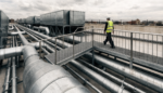 Engineer walking a rooftop step over platform above pipework and HVAC plant on a commercial building